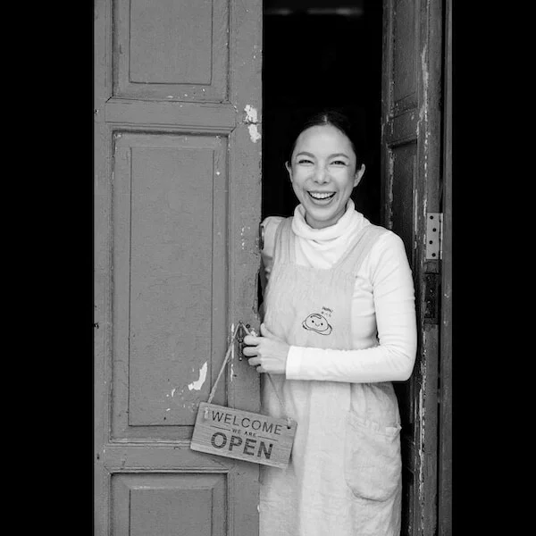 Black and white photo of a woman smiling through an open wooden door
